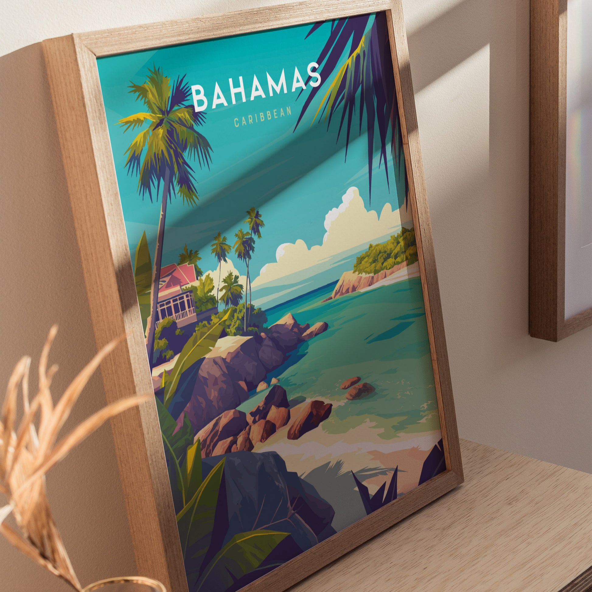 Framed Bahamas travel print depicting a tropical landscape with turquoise waters, rocky coastline, palm trees, and a red-roofed house under a bright blue sky.