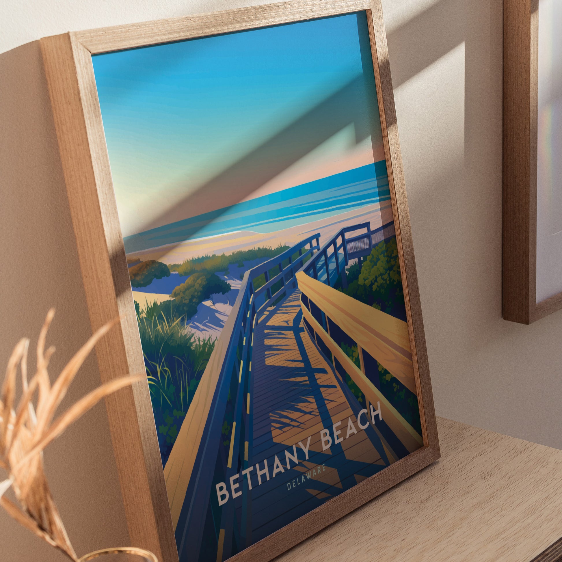 Framed poster depicting Bethany Beach, Delaware, shows a wooden boardwalk leading to dunes and the ocean under a blue sky, with shadows cast on the artwork.