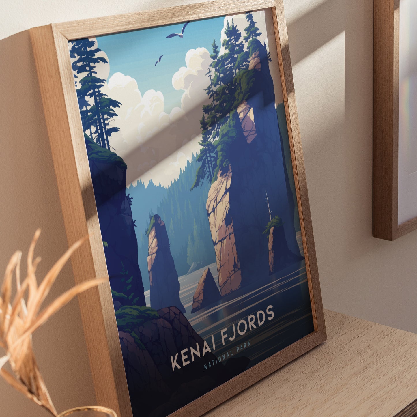 A framed Kenai Fjords National Park poster depicts towering rock formations and lush trees under a clear blue sky. Birds soar above, adding a sense of tranquility and natural beauty.