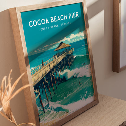 Framed poster of Cocoa Beach Pier in Florida, featuring a thatched-roof pavilion above turquoise waves, with a person walking along the pier. Displayed on a wooden surface.
