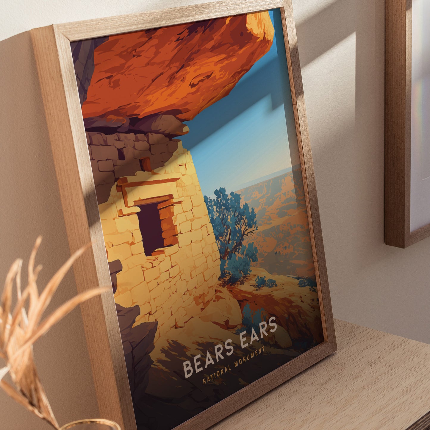 A framed poster of Bears Ears National Monument features a vibrant illustration of sandstone cliffs and ancient ruins, bathed in warm sunlight, set against a backdrop of desert landscape.