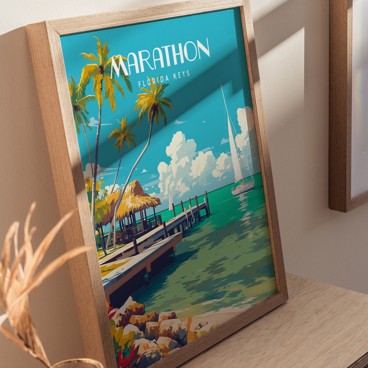 A framed poster of Marathon, Florida Keys features palm trees, a dock, and sailboats on turquoise water under a blue sky. The artwork is displayed on a wooden surface.