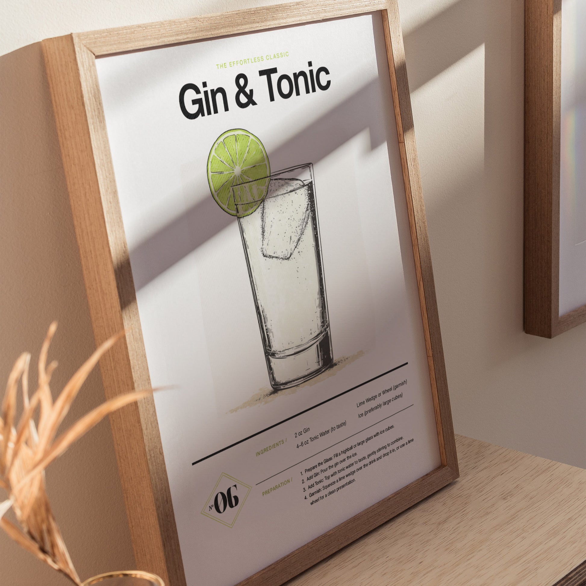 Framed Gin and Tonic cocktail poster featuring an illustrated drink with a lime slice, elegant typography, and a recipe list, displayed on a light wooden surface.