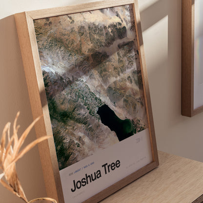 A framed poster featuring an aerial view of Joshua Tree, showcasing the desert landscape with rocky formations and a large body of water.