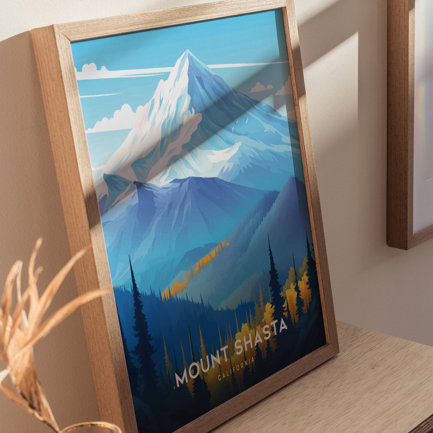 Framed poster of Mount Shasta with vibrant blue and orange hues, depicting the snow-capped peak and forested foothills, resting on a wooden surface.