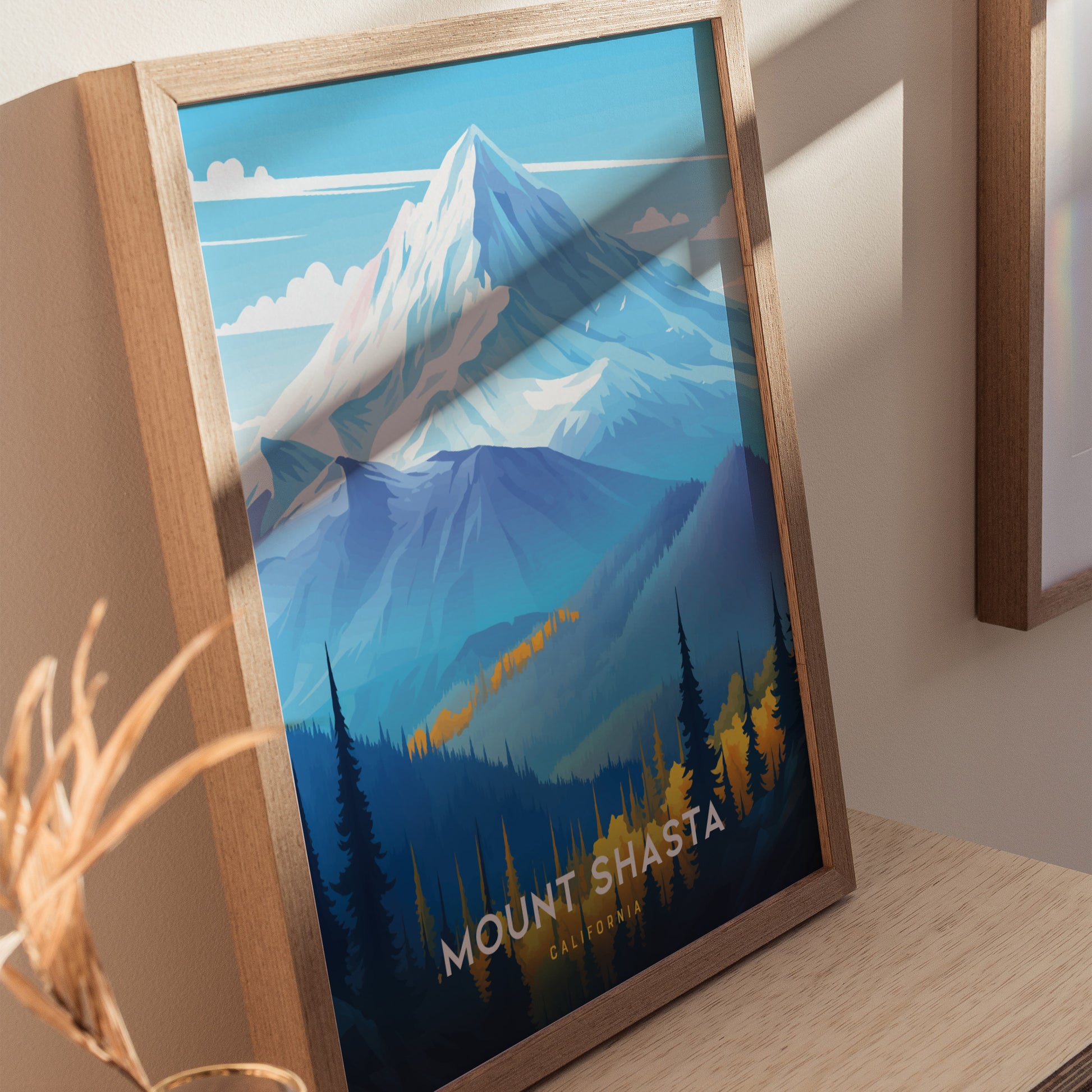 Framed poster of Mount Shasta with vibrant blue and orange hues, depicting the snow-capped peak and forested foothills, resting on a wooden surface.