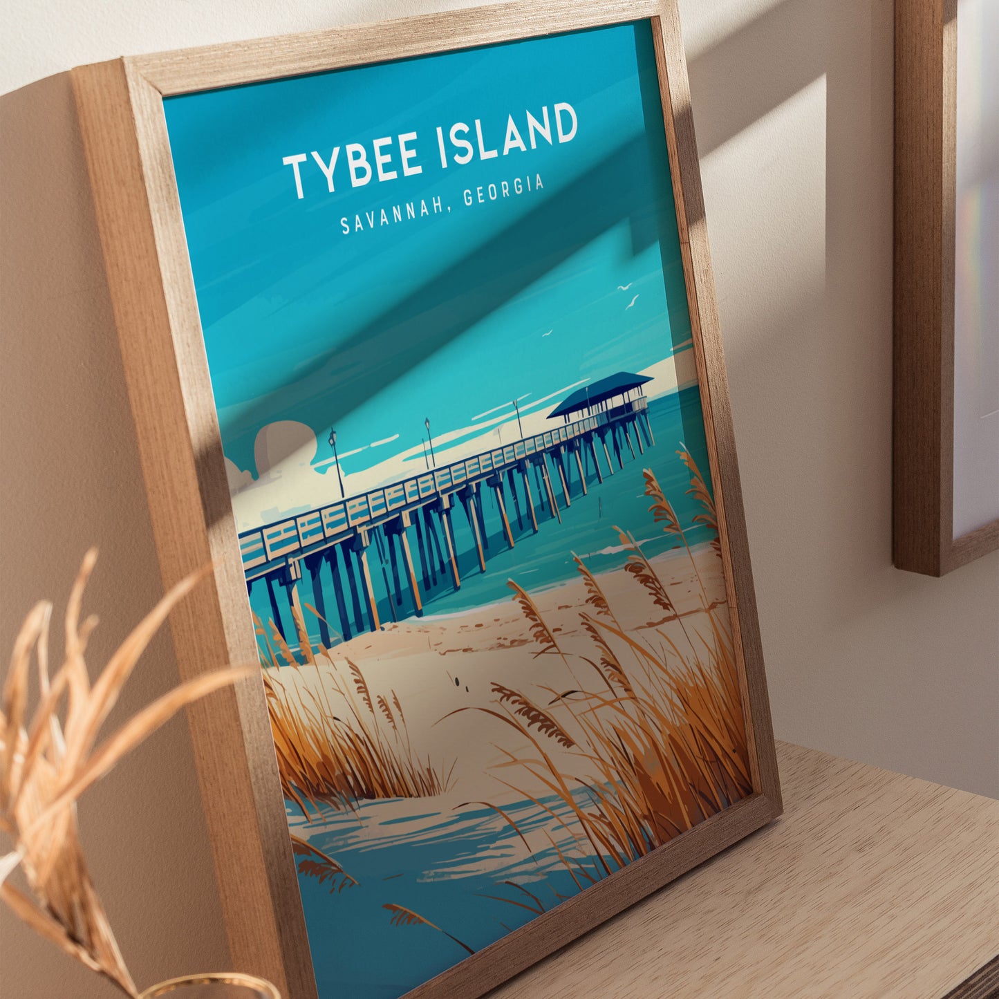 Framed Tybee Island poster depicting a wooden fishing pier stretching into the ocean, surrounded by sandy dunes and sea oats. The artwork is vibrant with blues and tans.