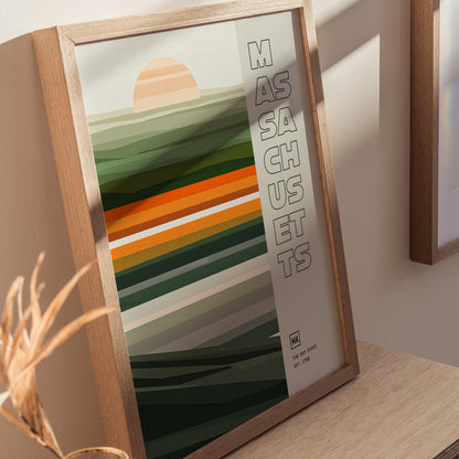 Framed Massachusetts poster featuring a minimalist design with horizontal stripes in green, orange, and brown tones, and a stylized sun. The word Massachusetts is vertically aligned on the right.