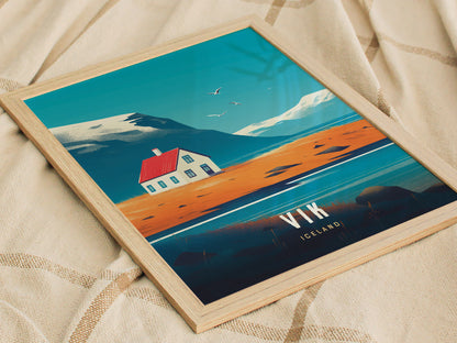 A framed poster featuring a stylized landscape with a house, red roof, and mountainous backdrop, titled Vik Iceland, resting on a soft, beige fabric surface.