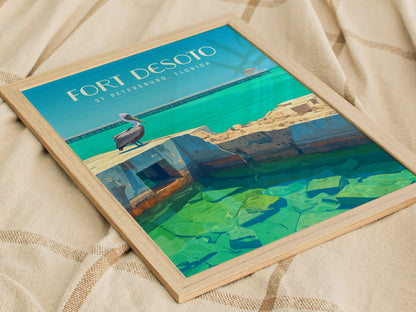 Framed illustration of Fort Desoto, featuring a pelican on ruins by turquoise water, with a pier in the background. The artwork lies on a textured beige surface.