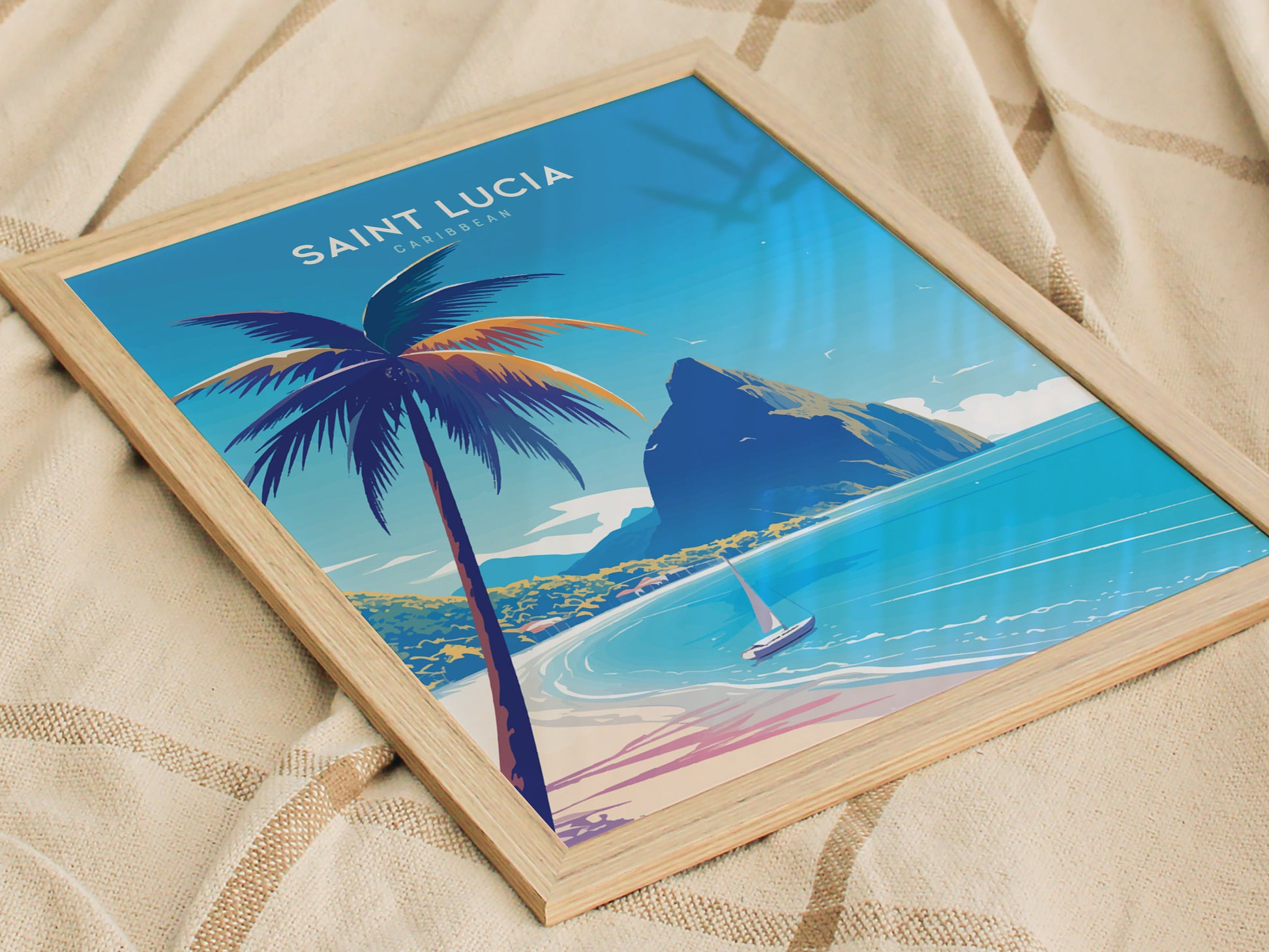 Framed poster depicting a tropical scene with a palm tree, turquoise waters, and a sailboat near a mountainous coastline, labeled Saint Lucia Caribbean, resting on a beige fabric background.