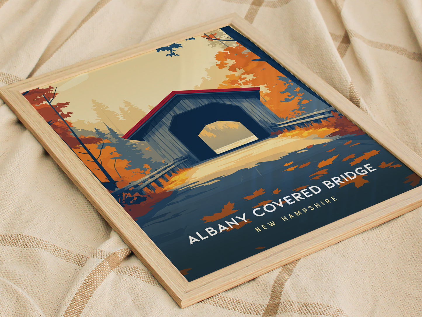 A framed poster of the Albany Covered Bridge in New Hampshire, featuring a vibrant autumn scene with colorful foliage in shades of orange and gold.