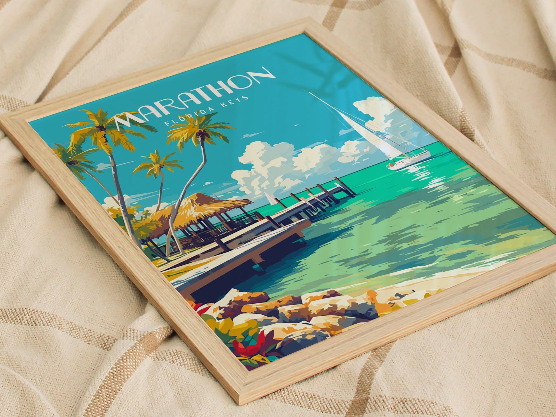 A framed poster of Marathon Florida Keys featuring palm trees, a pier, and turquoise waters, placed on a textured fabric surface. The artwork conveys a serene coastal scene.