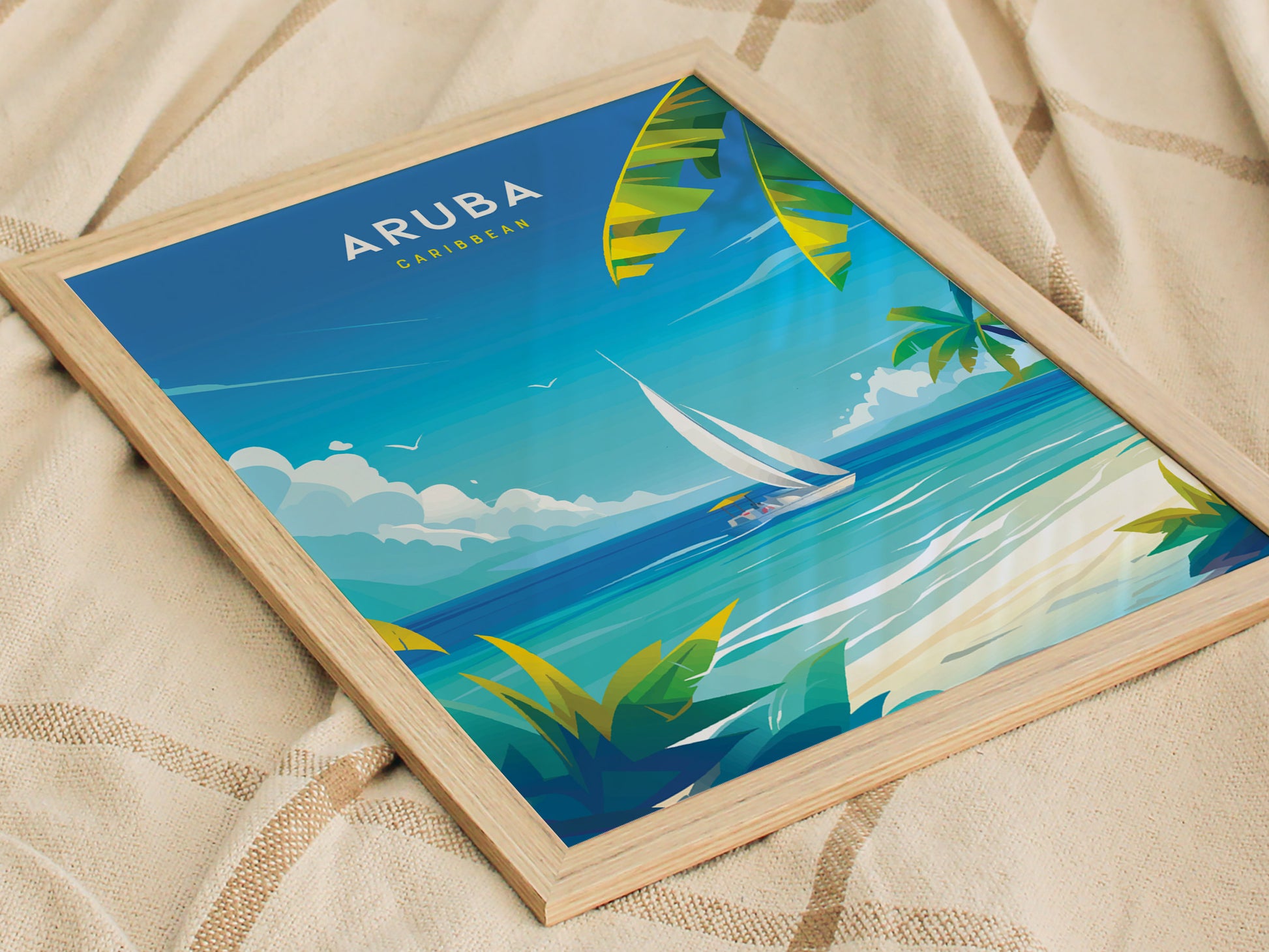 A framed poster featuring a vibrant illustration of Aruba with turquoise waters, a sailboat, and palm leaves, positioned on a textured beige fabric background.