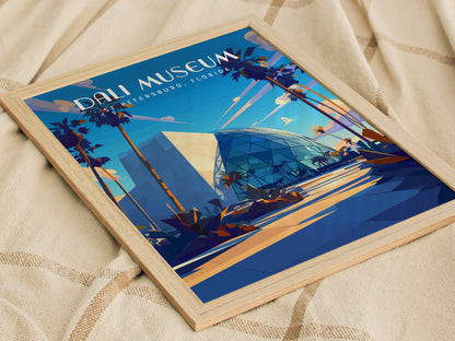 A framed poster of the Dali Museum in St. Petersburg, Florida, featuring stylized palm trees and modern architecture with a prominent glass atrium, resting on a textured fabric surface.