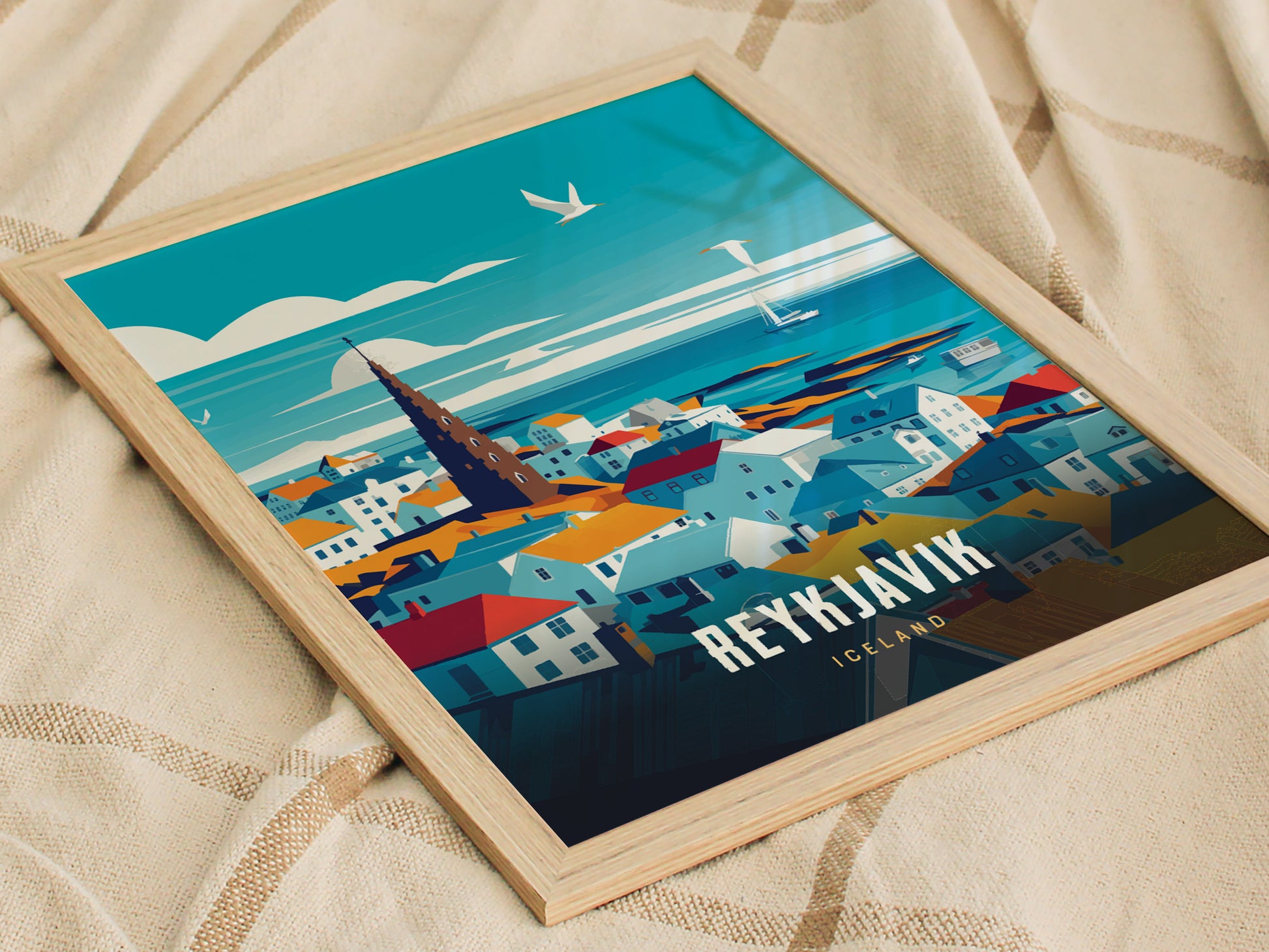 Framed travel poster of Reykjavík, Iceland, featuring colorful rooftops, the iconic Hallgrímskirkja church, and a vibrant sky with seagulls. The poster rests on a textured beige fabric.