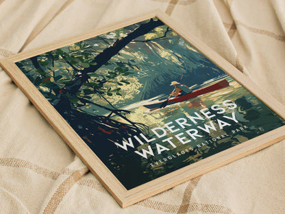 A framed poster titled Wilderness Waterway depicts a person canoeing through a serene waterway surrounded by lush mangrove forests, resting on a textured fabric surface.