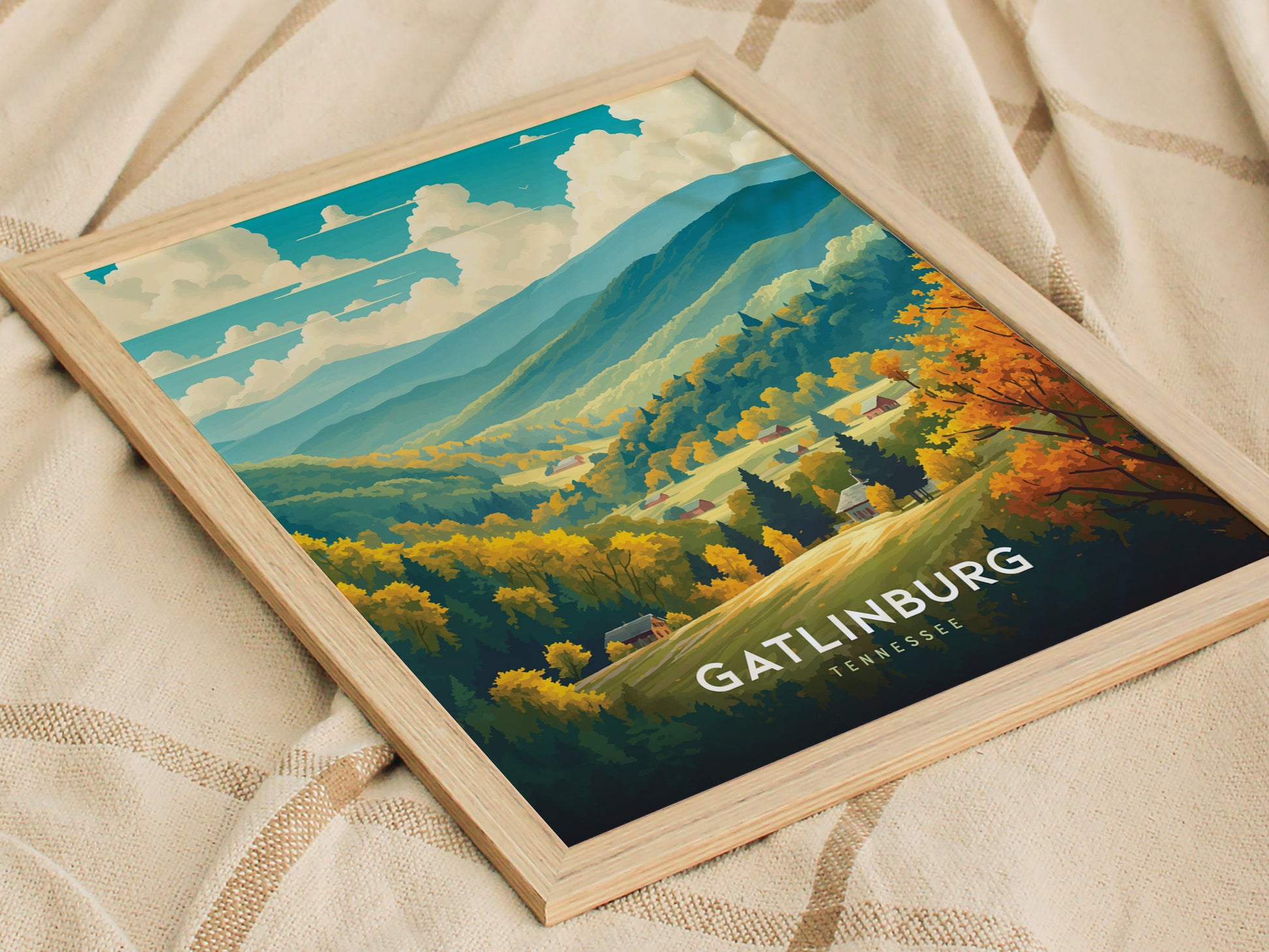 A framed poster of Gatlinburg, Tennessee, showcasing a vibrant landscape with lush forests, rolling hills, and clear skies, placed on a textured beige fabric surface.