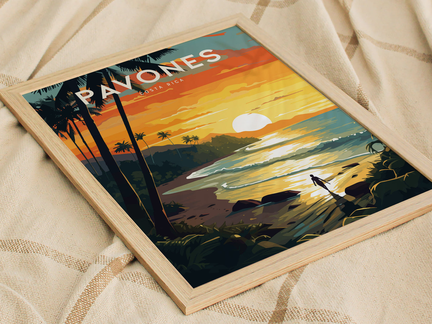A framed poster depicting a vibrant sunset over a tropical beach with palm trees and a lone surfer walking along the shore, placed on a textured fabric surface.