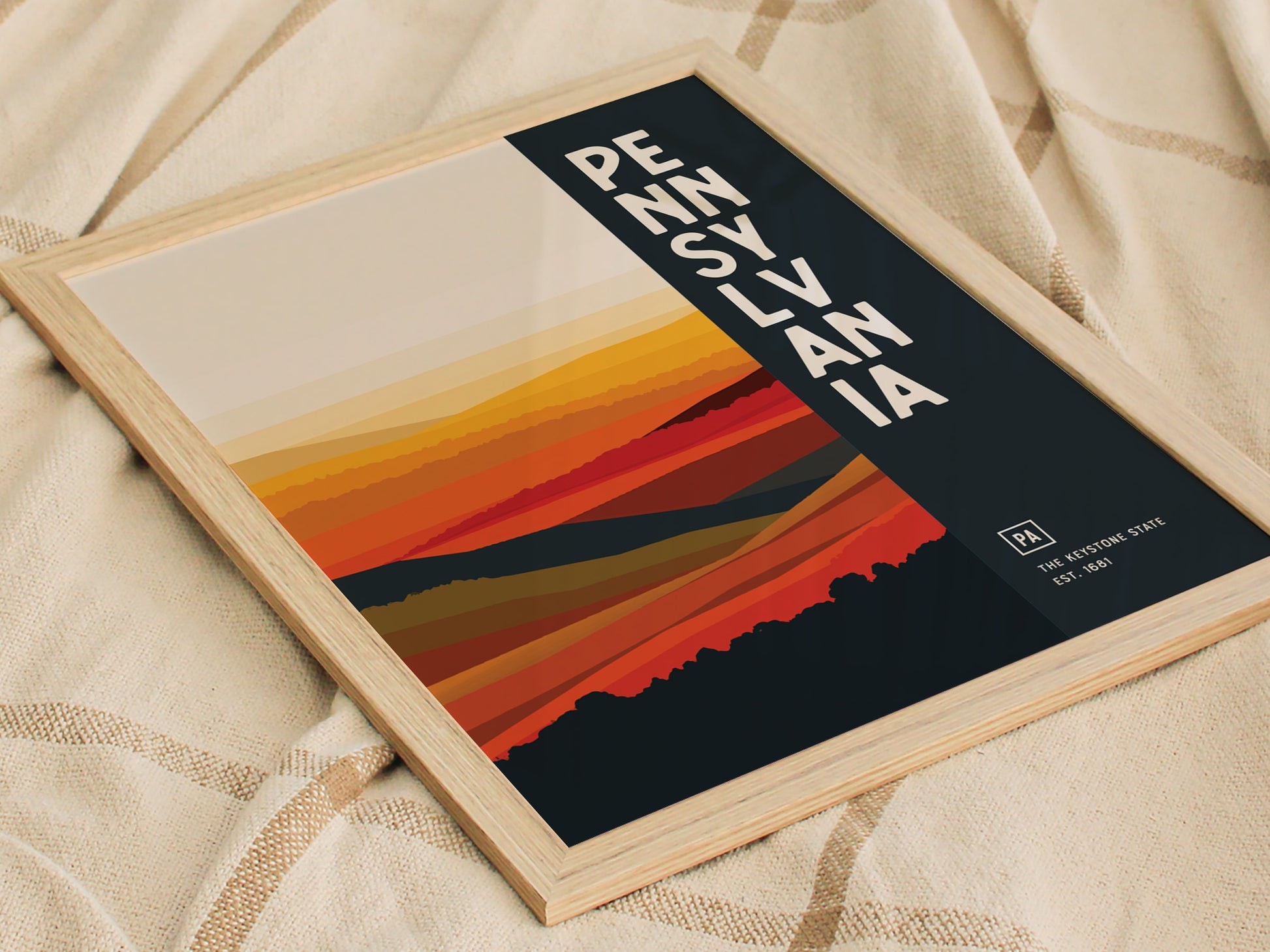This image shows a framed abstract Pennsylvania Keystone State poster with bold text and vibrant orange and red layers, set against a beige fabric background.