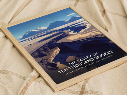 Framed poster depicting the Valley of Ten Thousand Smokes with a dramatic landscape of ash-covered valleys and mountains, set against a blue sky, displayed on a beige fabric.