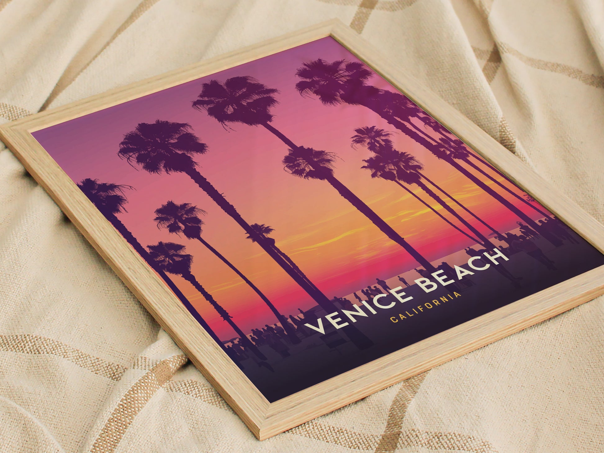 Framed poster of Venice Beach with palm trees silhouetted against a vibrant sunset of purples, pinks, and oranges. The text Venice Beach California is visible on the artwork.