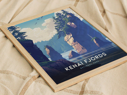 Framed poster featuring an illustrated landscape of Kenai Fjords National Park, displaying rocky cliffs, pine trees, and a serene ocean view, placed on a textured fabric surface.