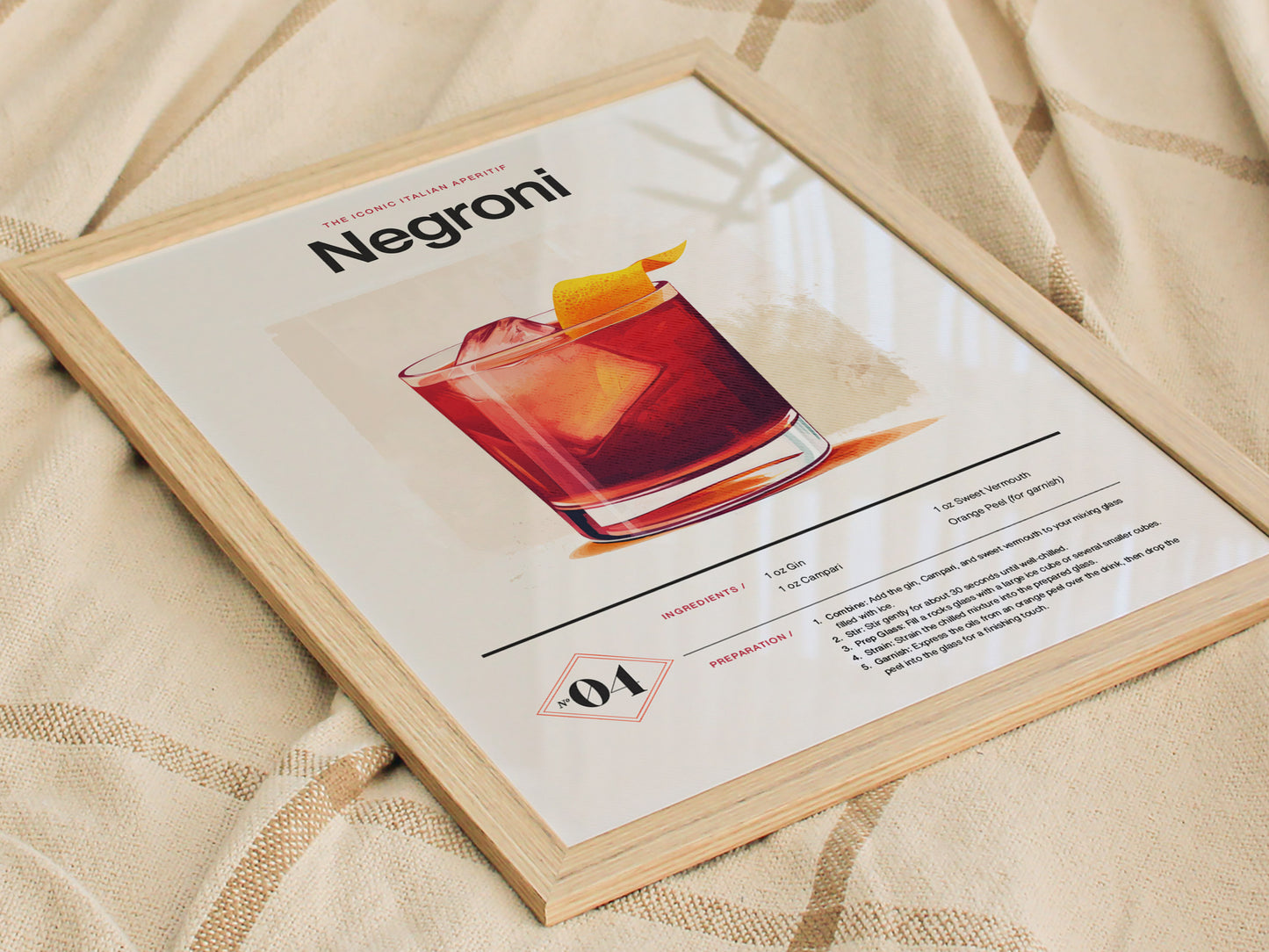 A framed Negroni cocktail poster lies on a beige fabric. The poster features an illustration of the drink with ingredients and preparation instructions.