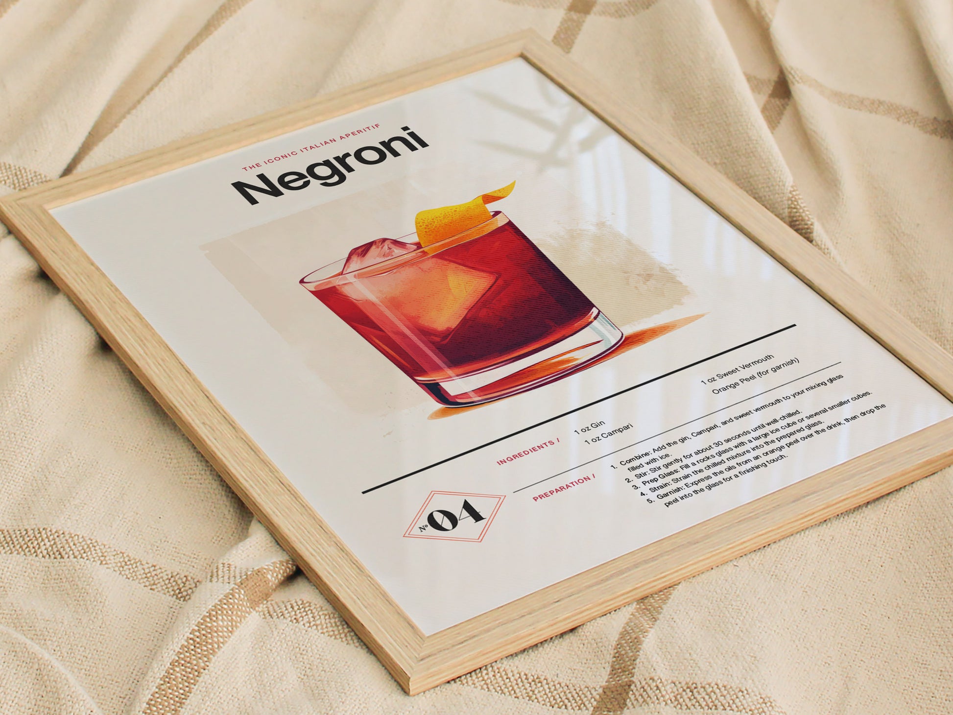 A framed Negroni cocktail poster lies on a beige fabric. The poster features an illustration of the drink with ingredients and preparation instructions.