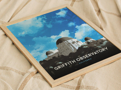 A framed poster of Griffith Observatory against a vibrant blue sky is displayed on a beige fabric background. The observatorys domes are illustrated in a clean, modern style.