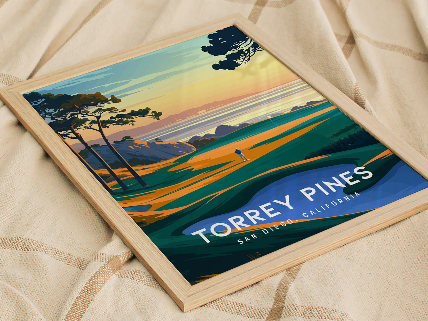 A framed poster of Torrey Pines in San Diego, California, features a vibrant golf course scene with coastal cliffs and a sunset over the ocean.