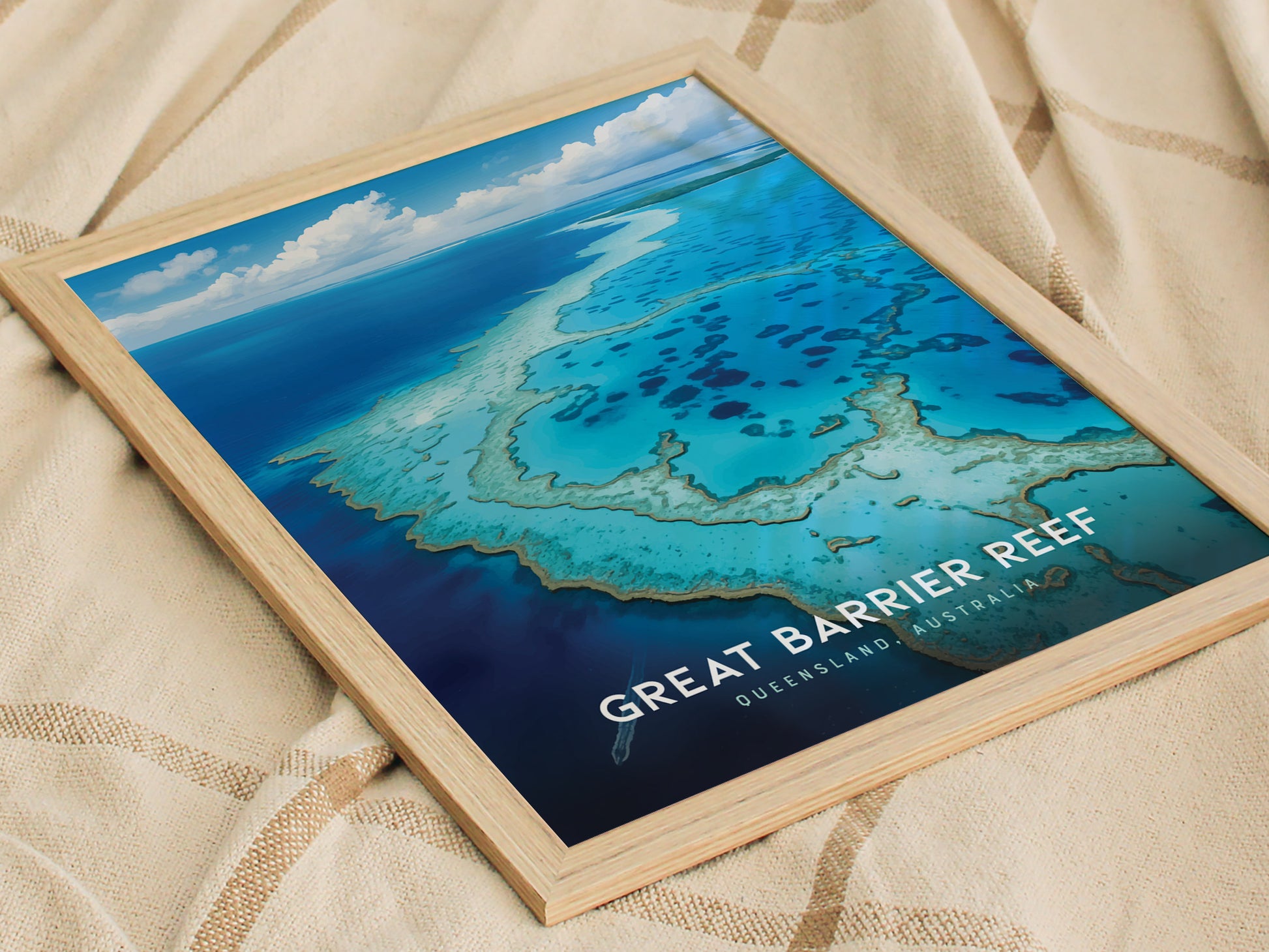 A framed poster of the Great Barrier Reef lies on a textured fabric surface. It features vivid blue waters and coral formations under a partly cloudy sky.