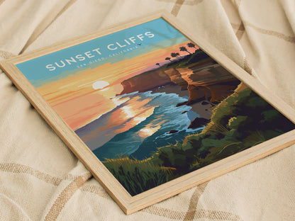 Framed poster depicting a vibrant sunset over cliffs and ocean waves, with palm trees silhouetted against the sky. The artwork is placed on a textured beige fabric.