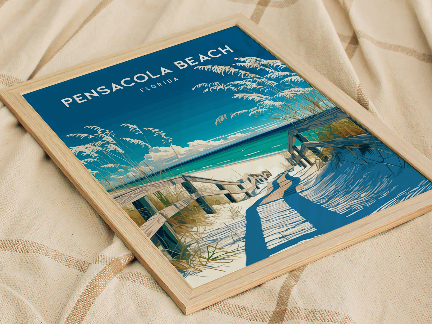 Framed poster of Pensacola Beach, Florida, depicting a wooden boardwalk leading to a sandy beach with sea oats and a vibrant blue sky, resting on a textured fabric surface.