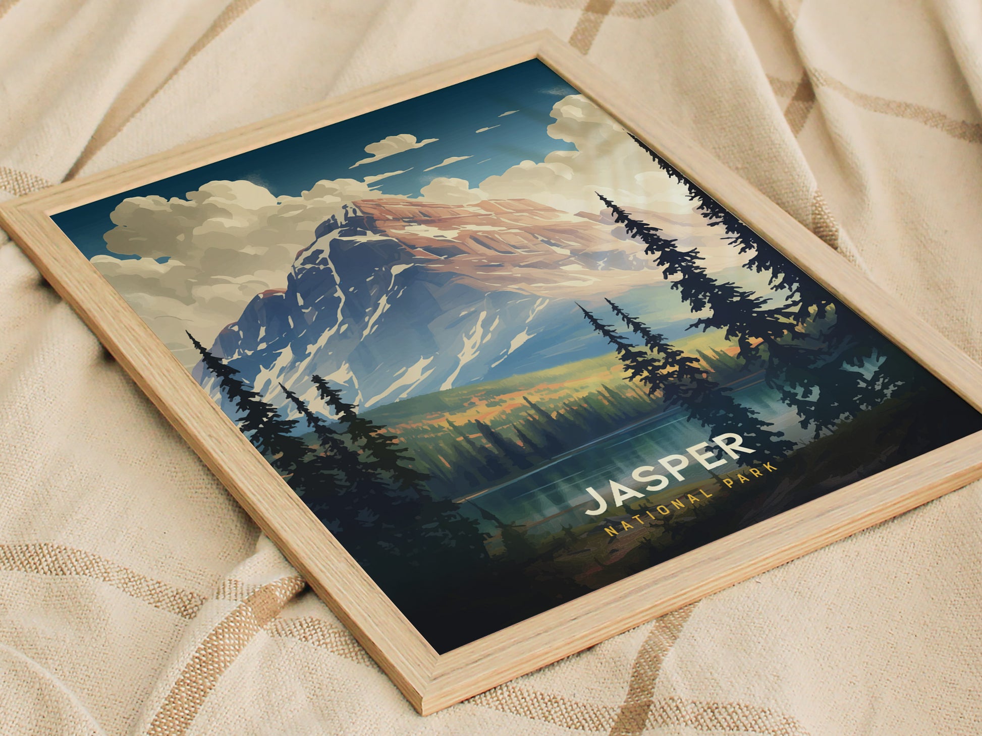 Framed poster of Jasper National Park featuring a majestic snow-capped mountain, lush evergreen trees, and a serene lake under a vibrant sky, resting on a beige fabric background.