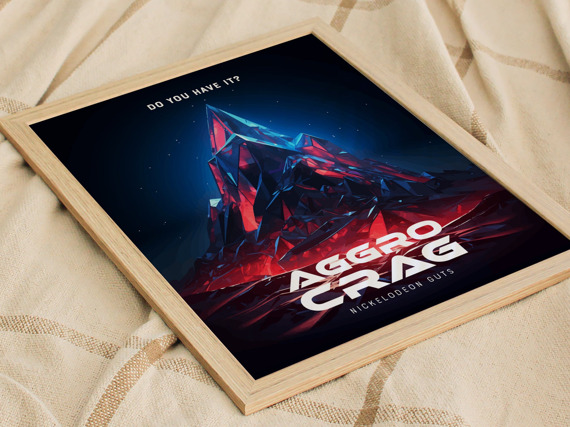A framed poster of the Aggro Crag from Nickelodeon GUTS, featuring bold geometric shapes in red and blue hues, resting on a textured fabric surface.