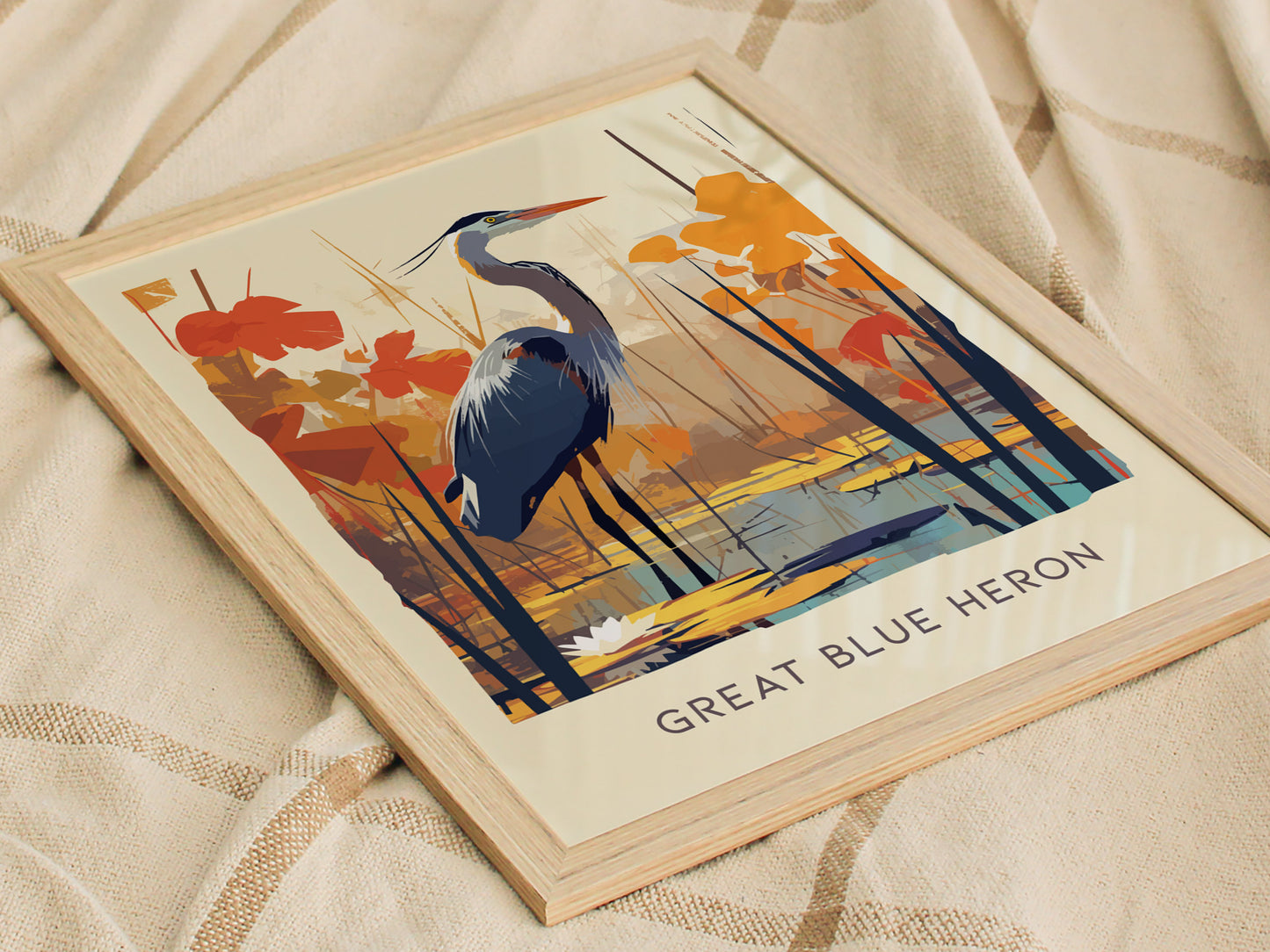 Framed poster featuring an illustrated Great Blue Heron amidst orange and blue abstract foliage, resting on a beige fabric background. The text Great Blue Heron is visible at the bottom.