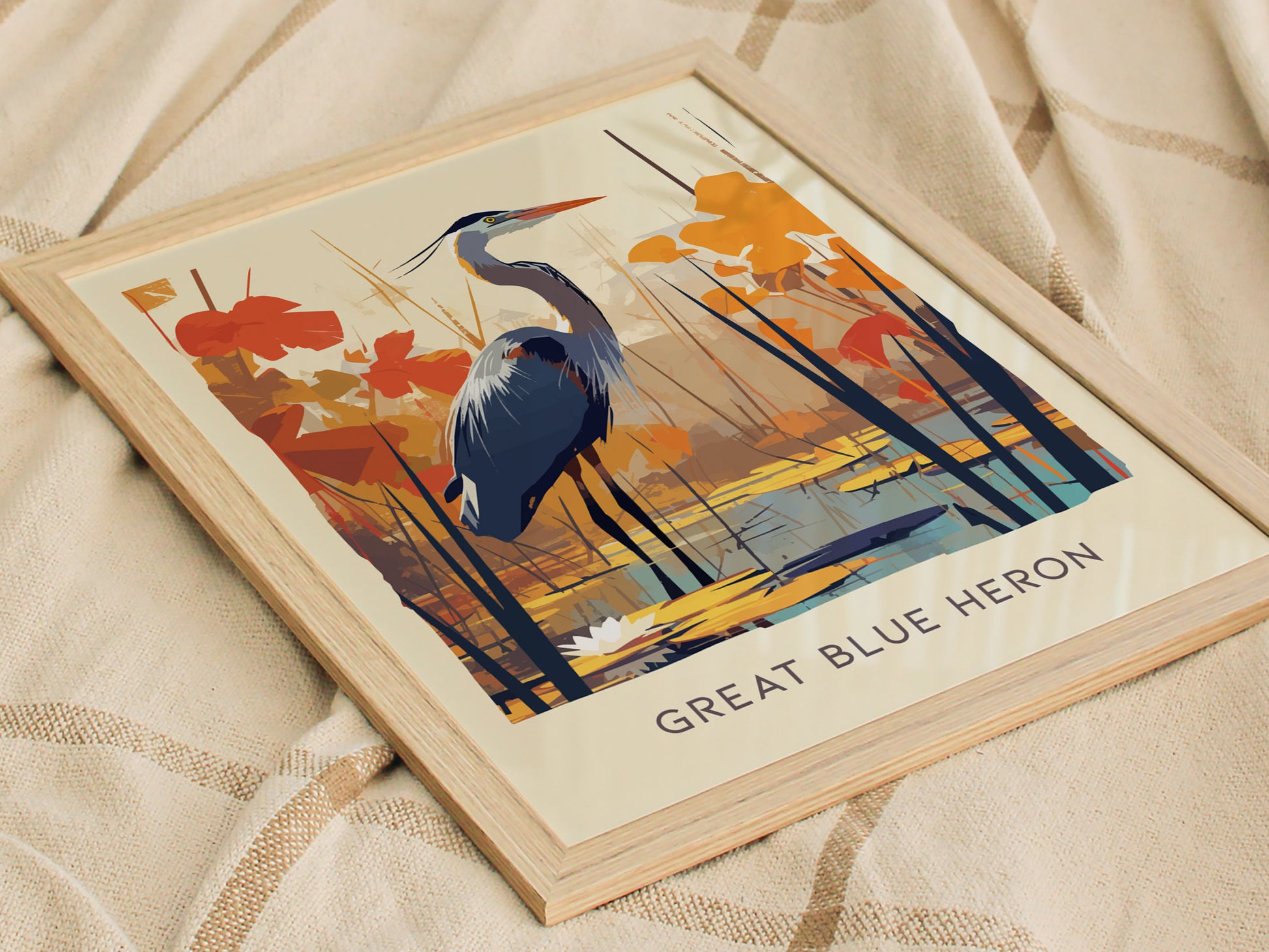 Framed poster featuring an illustrated Great Blue Heron amidst orange and blue abstract foliage, resting on a beige fabric background. The text Great Blue Heron is visible at the bottom.
