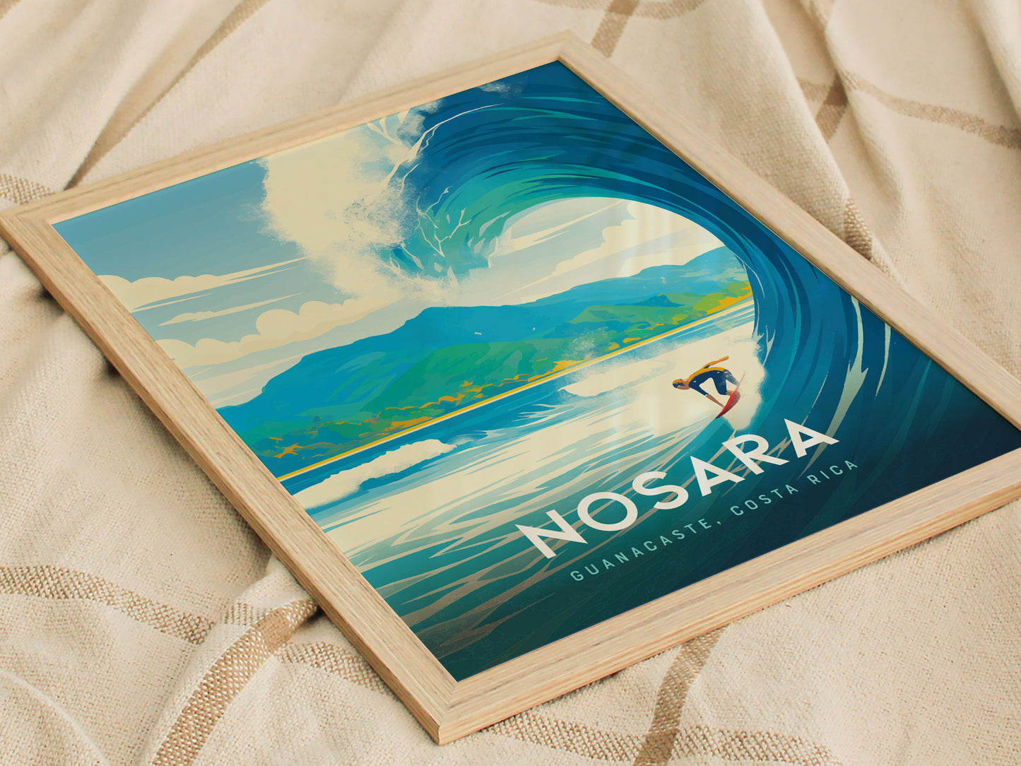 A framed Nosara, Costa Rica poster features a vibrant illustration of a surfer riding a wave with lush mountains in the background, placed on a textured fabric surface.