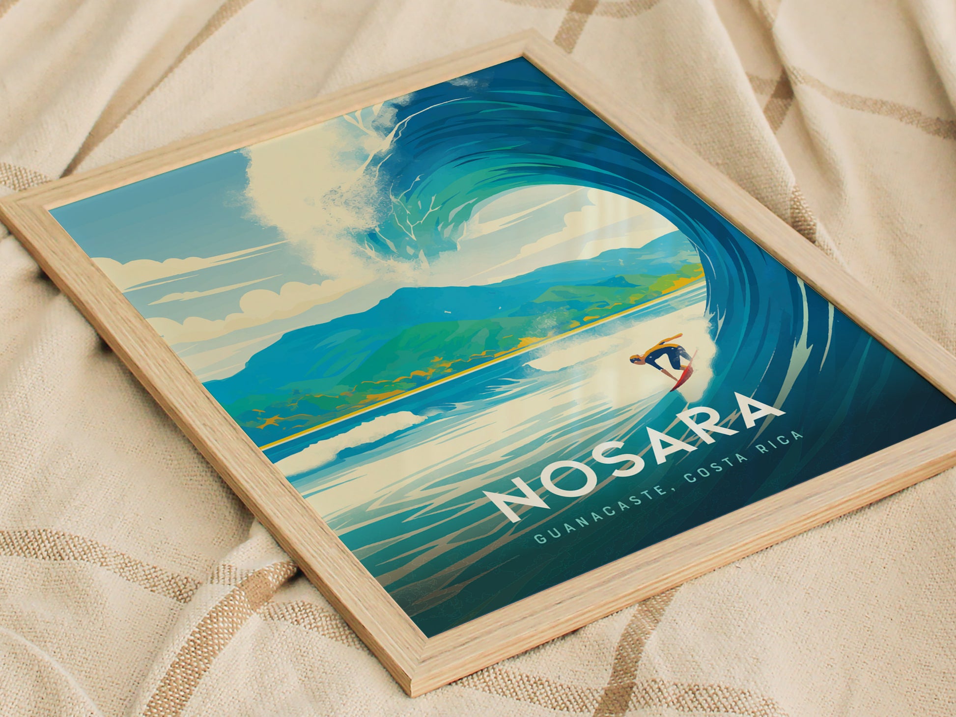 A framed Nosara, Costa Rica poster features a vibrant illustration of a surfer riding a wave with lush mountains in the background, placed on a textured fabric surface.