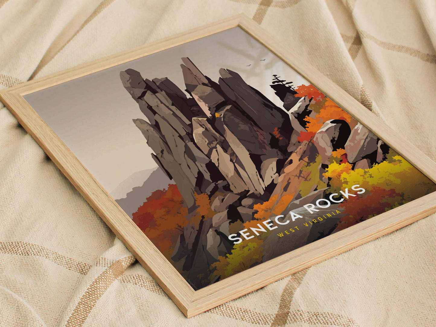 A framed poster of Seneca Rocks is placed on a beige fabric background, featuring a colorful illustration of the rock formation with autumn foliage and the text Seneca Rocks West.