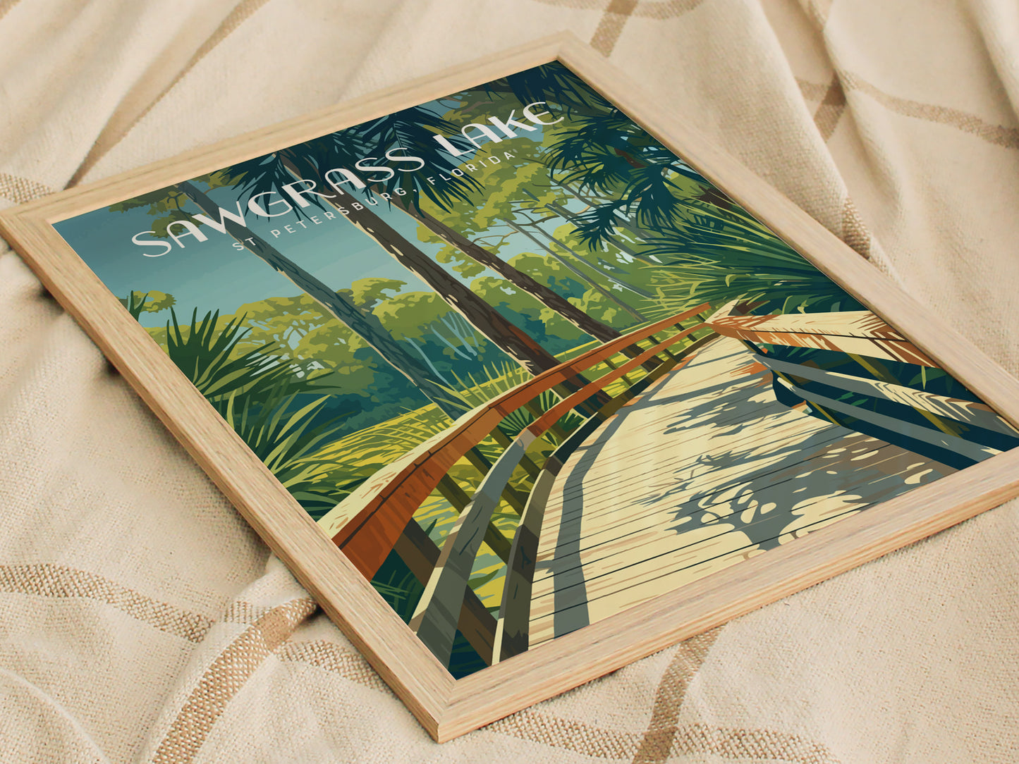 Framed poster of Sawgrass Lake with a wooden boardwalk winding through lush green foliage under a clear sky, placed on a textured beige surface.