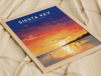 A framed poster of a Siesta Key sunset features vibrant oranges, purples, and yellows, with silhouettes of people and birds against a reflective shoreline.