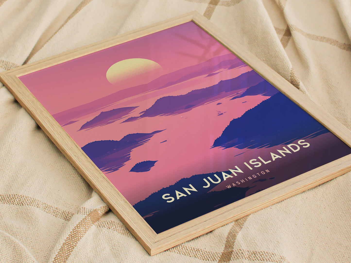 Framed poster of San Juan Islands with a vibrant pink and purple sunset over silhouettes of islands and water, resting on a cozy beige fabric background.