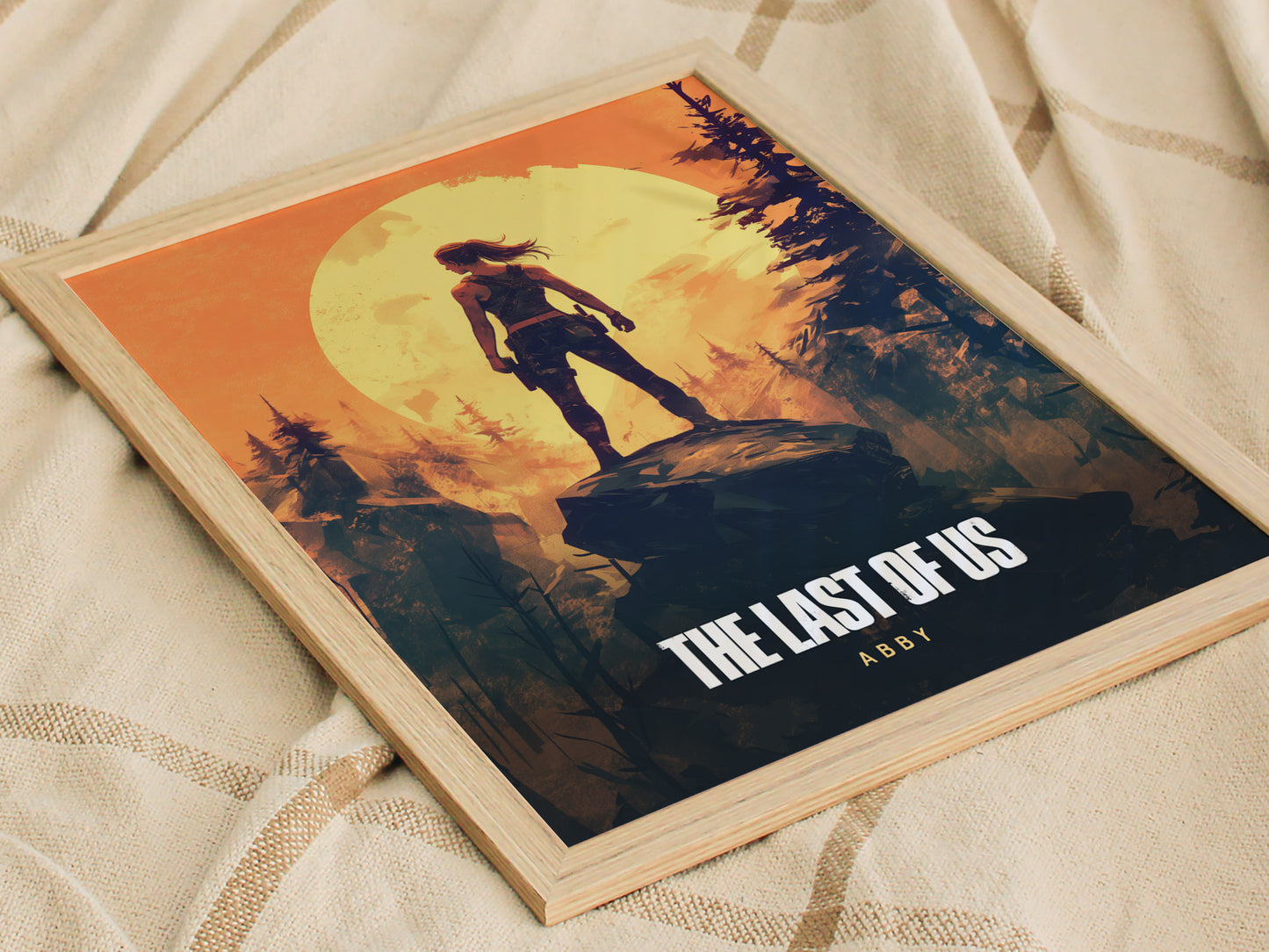 A framed poster of The Last of Us featuring a silhouette of a character standing on a rock against a large yellow moon and orange sky, placed on a beige.