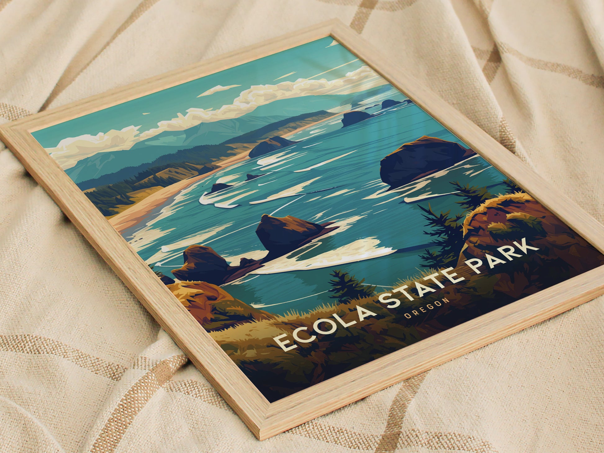 Framed poster of Ecola State Park featuring an illustration of Oregons coastal landscape with lush headlands, rugged cliffs, and the Pacific Ocean, resting on a textured fabric background.