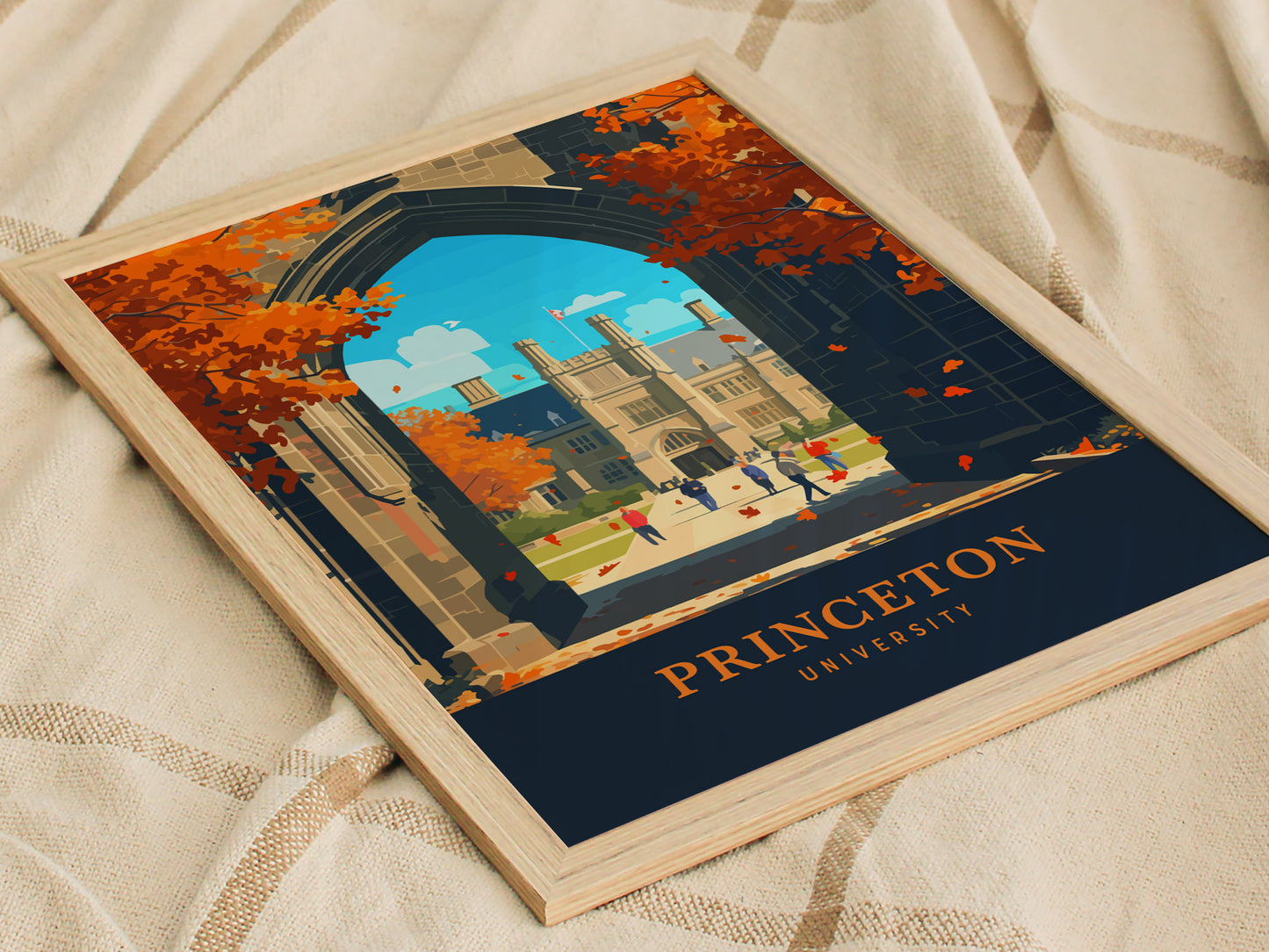 A framed poster of Princeton University features Gothic Revival architecture and autumn trees. The poster rests on a soft, textured fabric, showcasing vibrant colors and intricate details.