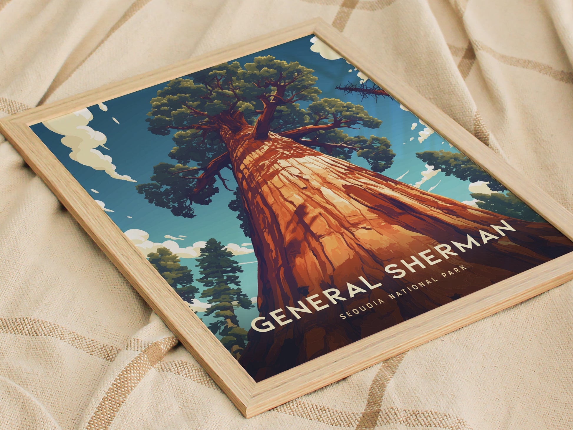 Framed poster of the General Sherman Tree from Sequoia National Park, showcasing a towering tree under a blue sky with clouds. The artwork rests on a beige fabric.