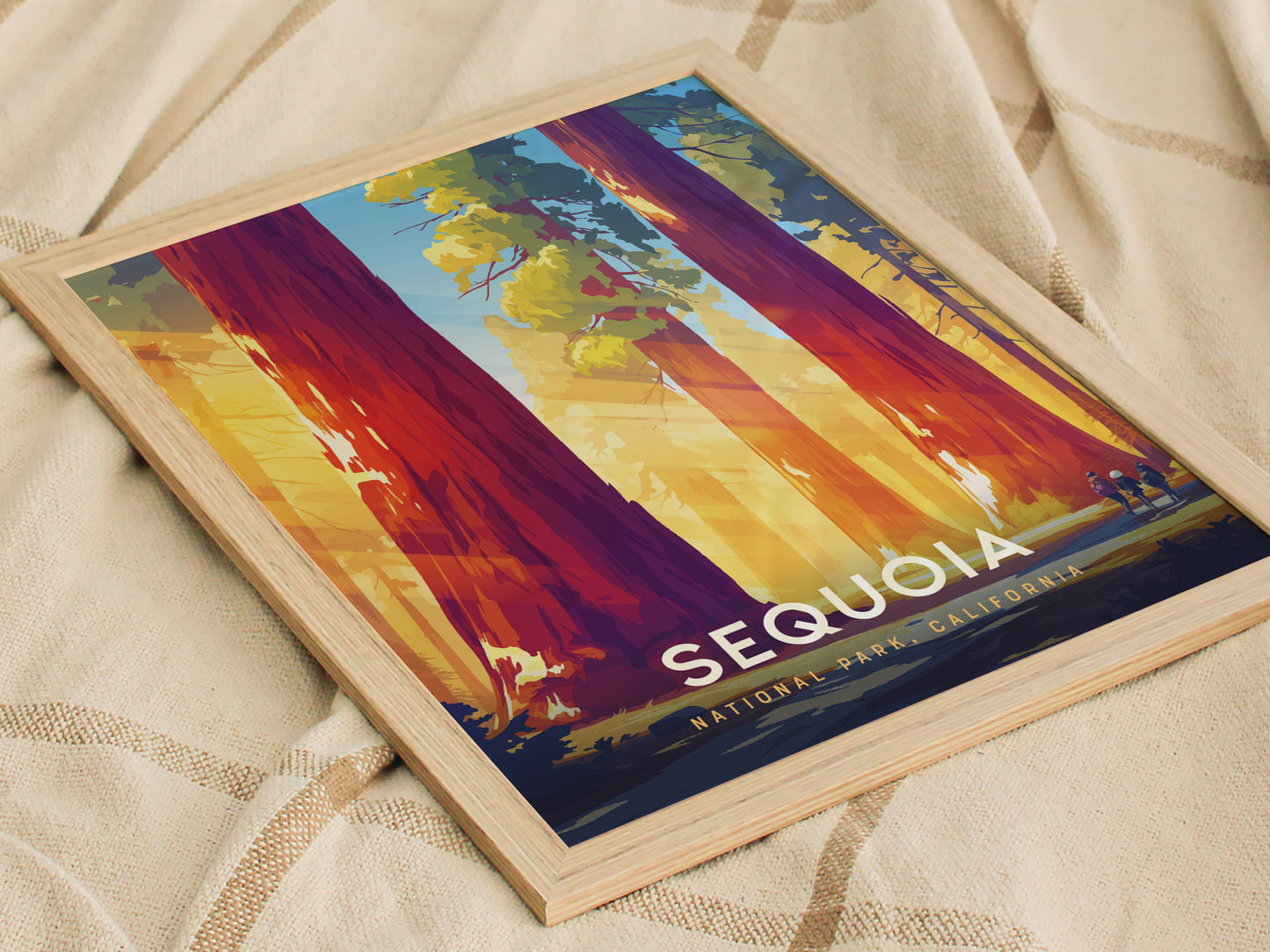 Framed poster featuring vibrant illustrations of towering sequoias with sunlight filtering through, labeled Sequoia National Park, California, resting on a textured beige fabric.
