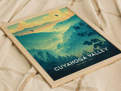 A framed poster of Cuyahoga Valley National Park displays a colorful illustration with rolling hills, trees, and birds against a vibrant sky, resting on a textured fabric surface.